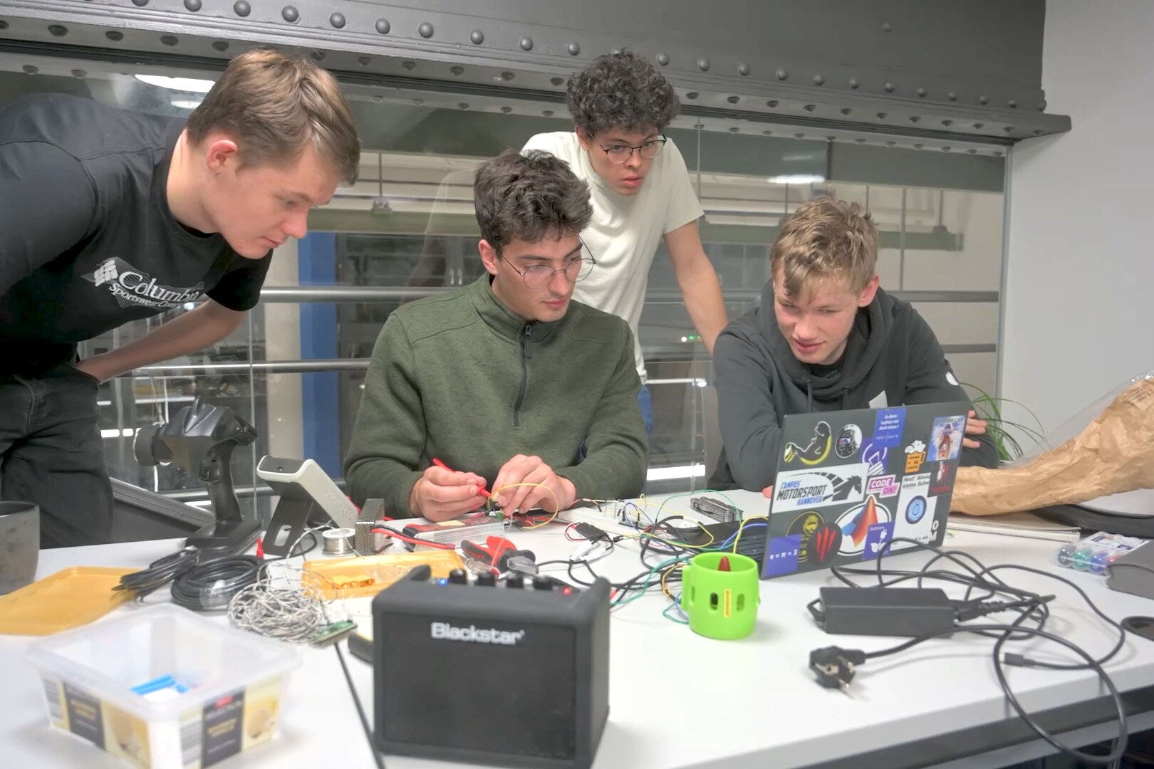 Team members soldering and testing electronics at the workbench