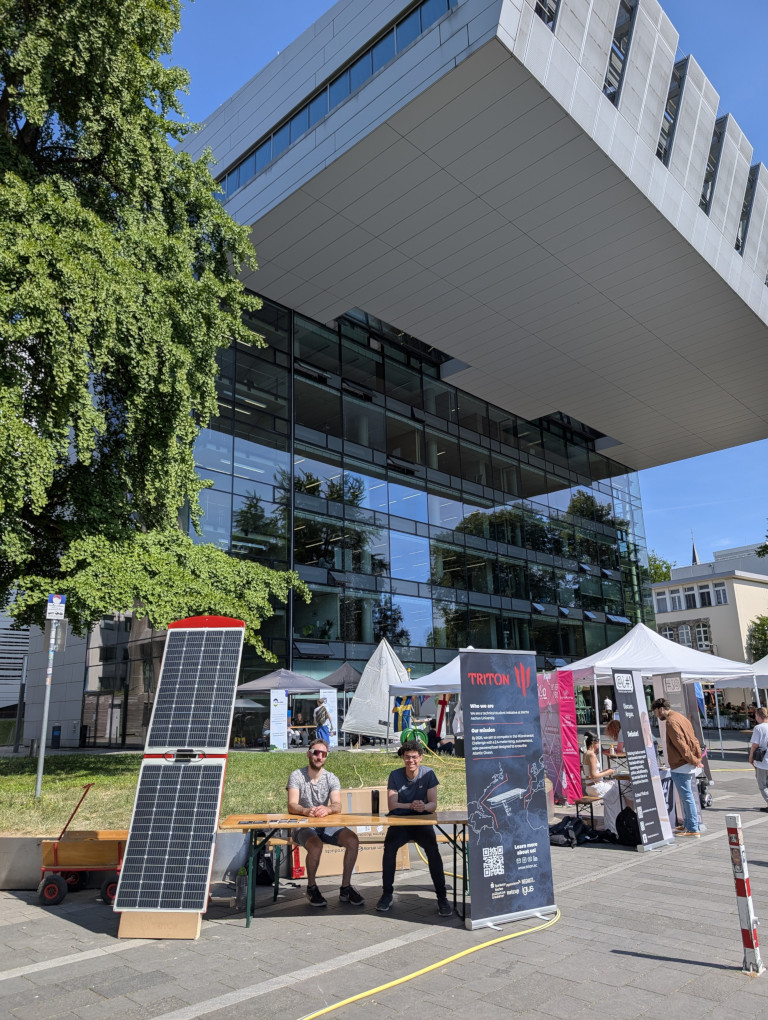 Image of Triton stand at TdsI with two people sitting at next to a solar powered boat.